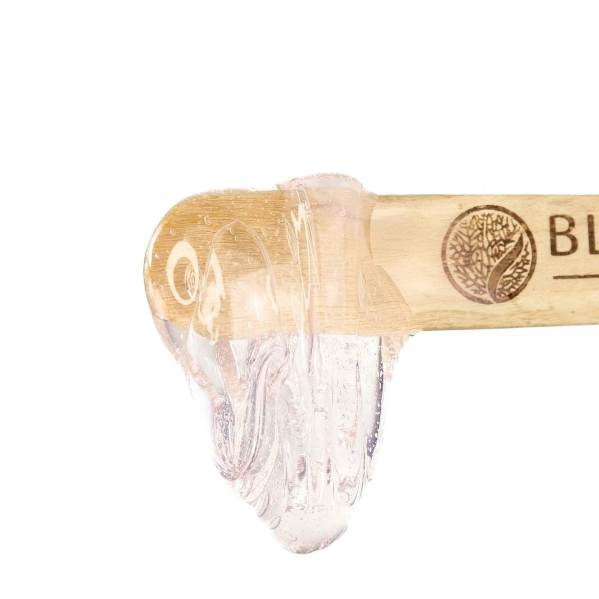 A wooden applicator coated with a clear, gel-like formula at its tip is shown against a white background, displaying a tree emblem and the partial word BLU. It represents precise waxing results with Black Coral Wax Mae Mae Hard Wax