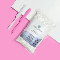 A 5lb Warmer + FREE Hot Wax from Black Coral Wax, filled with white wax beads, is shown on a pink and white background beside two waxing spatulas—one white and one pink.
