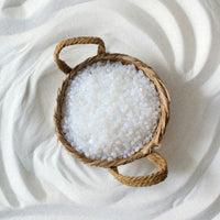 Woven basket with Mae Mae hard wax beads on a textured white surface