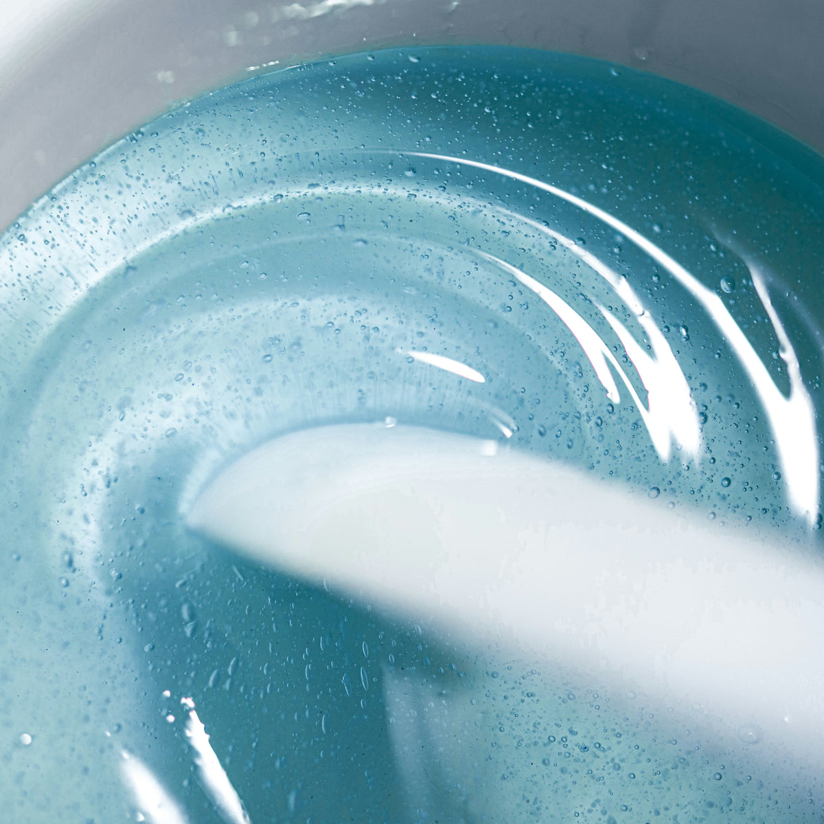 A close-up of  light blue Kai Hard Wax  and a wooden stick engraved with Black Coral Wax . Ideal for sensitive skin, the stick is partially submerged in the beads against a softly blurred background.
