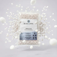 A clear bag of White Coral Wax by Black Coral Wax for sensitive skin is surrounded by loose hot wax beads floating against a light gray background.